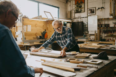 Senior male carpenter examining timber on workbench at repair shop - MASF35850