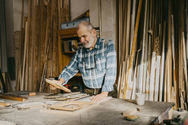 Ein älterer Schreiner prüft einen Bilderrahmen in der Werkstatt - MASF35857