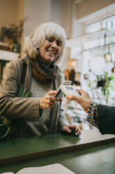 Ältere Frau, die beim Einkaufen im Geschäft mit der Tap-to-Pay-Methode bezahlt - MASF35879