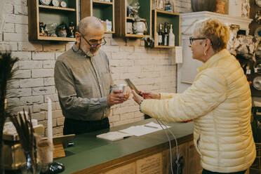Seitenansicht einer Kundin, die nach einem Einkauf in einem Ladengeschäft mit der Tap-to-Pay-Methode bezahlt - MASF35884