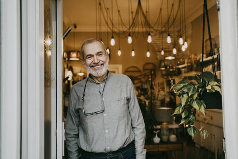 Portrait of happy senior male owner standing near door of interior shop - MASF35885