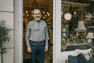 Happy male entrepreneur standing at entrance of home interior shop - MASF35887