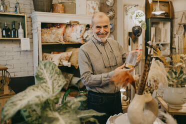 Glücklicher älterer männlicher Besitzer zeigt Glasdekor in einem Geschäft für Innenausstattung - MASF35900