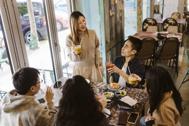 Smiling woman enjoying drinks with male and female friends at restaurant - MASF35913