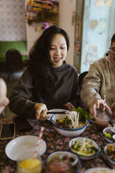 Lächelnde Frau nimmt Essen aus einer Schüssel, während sie im Restaurant sitzt - MASF35915