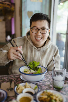 Porträt eines lächelnden jungen Mannes mit Essen und Stäbchen in einem Restaurant - MASF35916