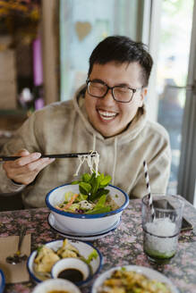 Glücklicher junger Mann, der im Restaurant mit Stäbchen isst - MASF35917