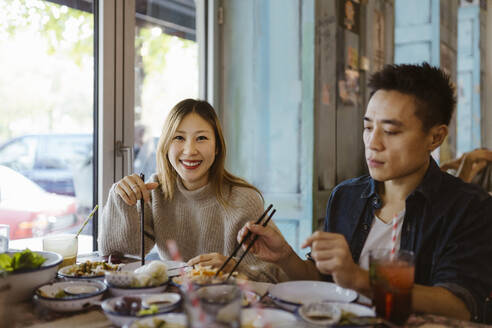 Porträt einer lächelnden Frau mit Stäbchen, die mit einem männlichen Freund im Restaurant isst - MASF35920
