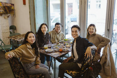 Portrait of happy male and female friends sitting together at restaurant - MASF35924