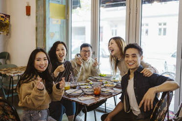 Happy multiracial male and female friends gesturing and laughing during lunch at restaurant - MASF35926