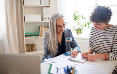 A senior woman volunteer helping Ukrainian woman to fill in forms at asylum centre. - HPIF07013