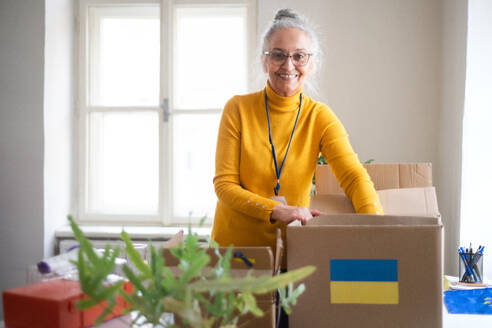 Eine ältere ehrenamtliche Mitarbeiterin packt einen Karton mit humanitärer Hilfe für ukrainische Flüchtlinge im Büro - HPIF07030