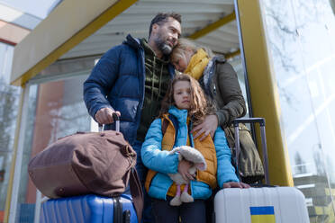 An Ukrainian refugee family with luggage at railway station together, Ukrainian war concept. - HPIF07035
