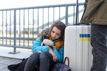 A sad Ukrainian immigrant child with luggage waiting at train station, Ukrainian war concept. - HPIF07037