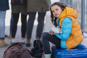 A sad Ukrainian immigrant child with luggage waiting at train station, Ukrainian war concept. - HPIF07038