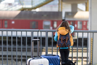 A rear view of Ukrainian immigrant child with luggage waiting at train station, Ukrainian war concept. - HPIF07042