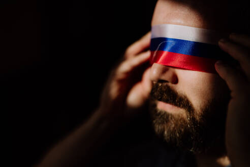 Ein Mann mit russischer Flagge Augenbinde auf schwarzem Hintergrund, russische Propaganda geschlossen Menschen die Augen Konzept. - HPIF07053