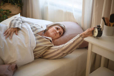 Eine übergewichtige Frau wacht im Bett auf und schaltet den Wecker zu Hause aus. - HPIF07078