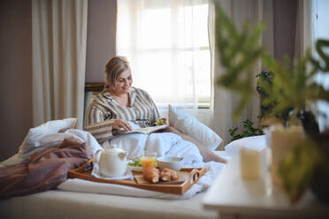 Eine glückliche übergewichtige Frau mit Kopfhörern und Smartphone frühstückt zu Hause im Bett. - HPIF07080