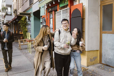 Cheerful male and female friends talking while walking on sidewalk - MASF35940