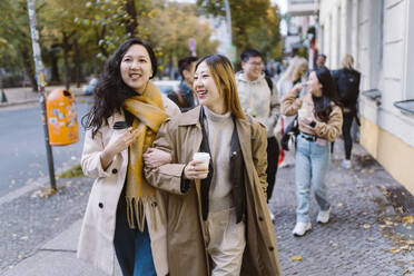 Lächelnde Freundinnen, die Arm in Arm auf dem Bürgersteig gehen - MASF35942