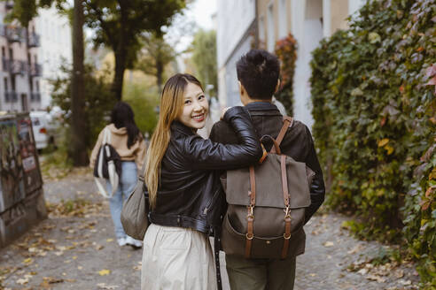 Rückansicht eines Mannes, der mit einer Freundin auf dem Gehweg spazieren geht und über die Schulter schaut - MASF35980