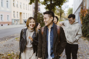 Männliche und weibliche Freunde lachen beim Gehen auf dem Bürgersteig - MASF35981