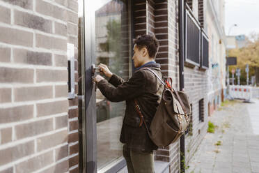 Man wearing backpack while locking apartment door - MASF35986