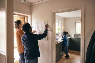 Father and mother hanging painting on wall with son standing in kitchen at home - MASF35999