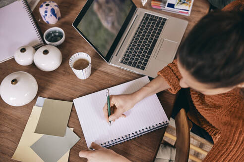 High angle view of female freelancer preparing to-do list in spiral book while sitting with laptop at home - MASF36002