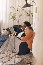 Mann und Frau lesen Bücher, während sie zu Hause auf dem Sofa sitzen - MASF36014