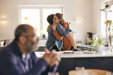 Smiling woman embracing mother-in-law while standing in kitchen at home - MASF36040