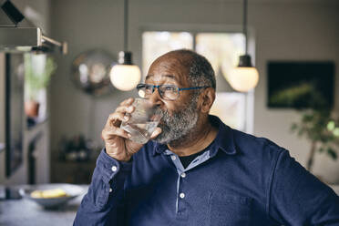 Nachdenklicher älterer Mann trinkt zu Hause Wasser - MASF36064