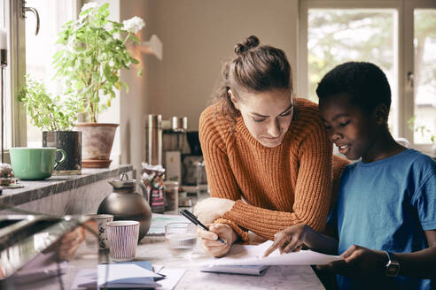 Mother assisting son while doing homework at home - MASF36068