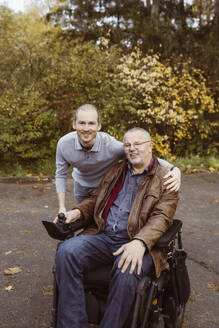 Porträt eines lächelnden jungen Mannes, der seinen Vater im motorisierten Rollstuhl umarmt - MASF36104