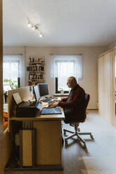 Seitenansicht eines älteren Mannes, der einen Computer am Schreibtisch im Heimbüro benutzt - MASF36112