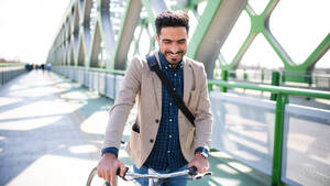 Ein junger Geschäftsmann mit Fahrrad auf dem Weg zur Arbeit in der Stadt, zu Fuß auf einer Brücke. - HPIF07087