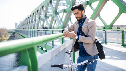 Portrait of young business man commuter with bicycle going to work outdoors in city, using smartphone. - HPIF07089