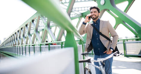 Porträt eines jungen Geschäftsmannes, der mit dem Fahrrad zur Arbeit in der Stadt fährt und dabei sein Smartphone benutzt. - HPIF07091