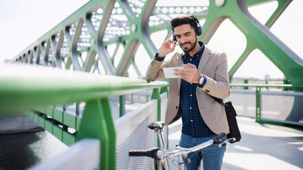 Ein junger Geschäftsmann pendelt mit dem Fahrrad zur Arbeit in der Stadt, Videoanruf auf dem Smartphone. - HPIF07092