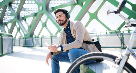 Portrait of young business man commuter with bicycle on the way to work outdoors in city, using smartphone. - HPIF07093