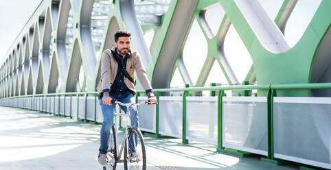 Ein junger Geschäftsmann auf dem Weg zur Arbeit mit dem Fahrrad in der Stadt, auf einer Brücke fahrend. - HPIF07097