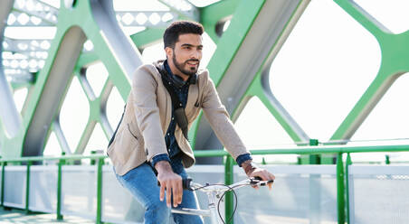 Ein junger Geschäftsmann auf dem Weg zur Arbeit mit dem Fahrrad in der Stadt, auf einer Brücke fahrend. - HPIF07098