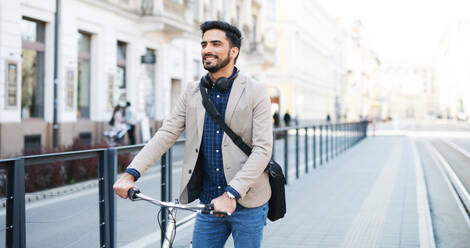 Portrait of young business man commuter with bicycle going to work outdoors in city. - HPIF07099