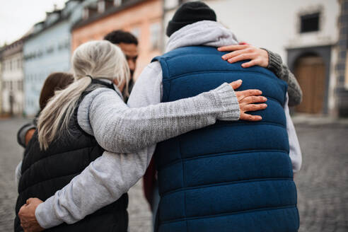 A rear view of community service volunteers hugging together outdoors in street - HPIF07149