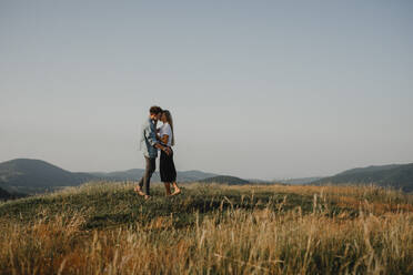 Seitenansicht eines jungen Paares bei einem Spaziergang in der Natur bei Sonnenuntergang auf dem Lande, das sich küsst. - HPIF07154