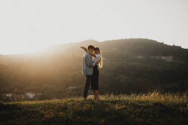 Side view of young couple on a walk in nature at sunset in countryside, hugging. - HPIF07158