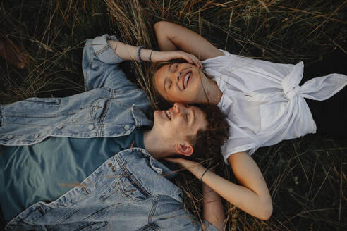 A young couple on a walk in nature in countryside, lying in grass laughing. - HPIF07163