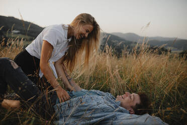 Ein junges Paar auf einem Spaziergang in der Natur auf dem Land, im Gras liegend und lachend. - HPIF07167