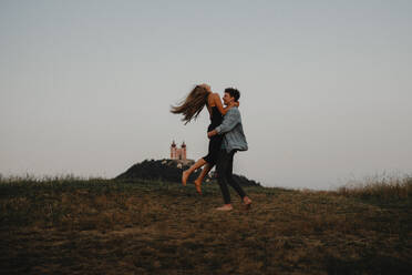 Side view of young couple on a walk in nature at dusk in countryside, having fun hugging. - HPIF07172